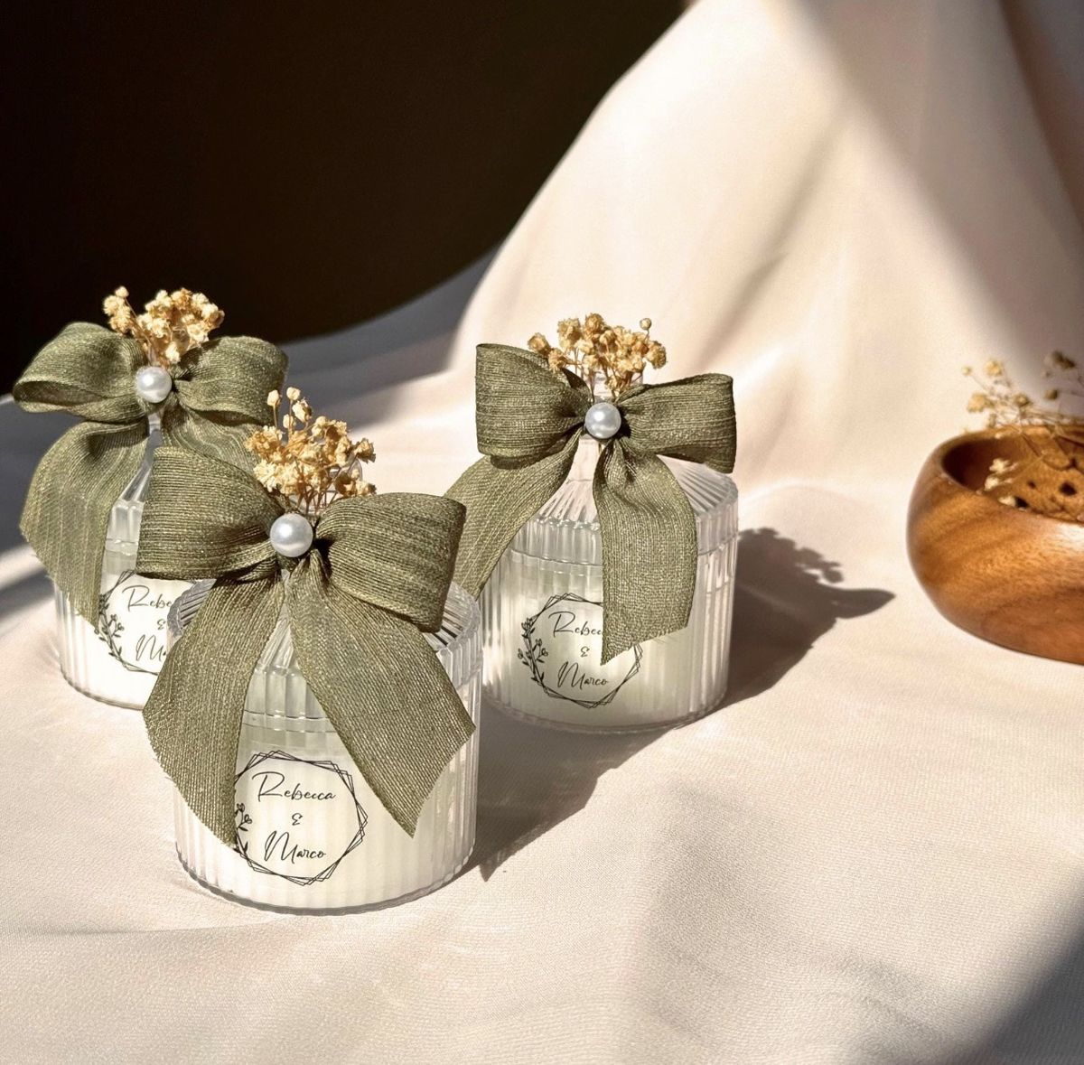 Three ribbed glass candles with sage green bows, pearl pins and dried gypsophila, labelled Rebecca & Marco